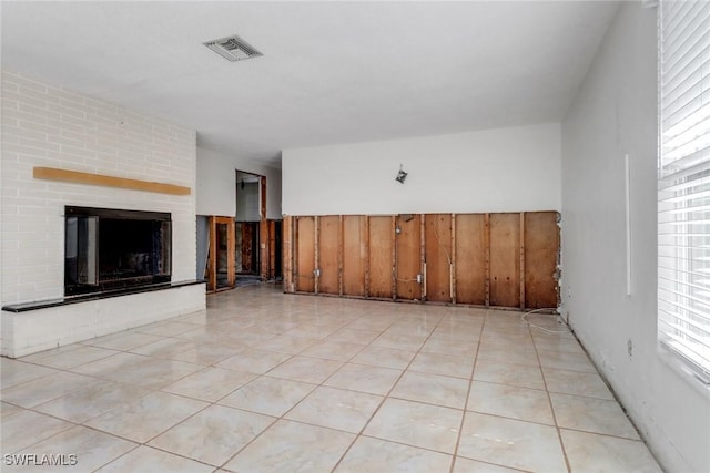 unfurnished living room with light tile patterned floors, a brick fireplace, and visible vents