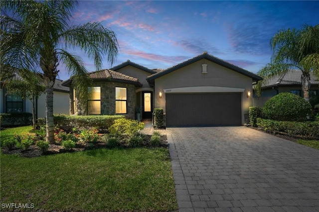 view of front facade featuring stucco siding, a front lawn, decorative driveway, stone siding, and a garage