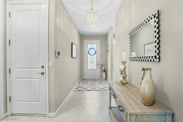 doorway with tile patterned floors, a notable chandelier, and baseboards