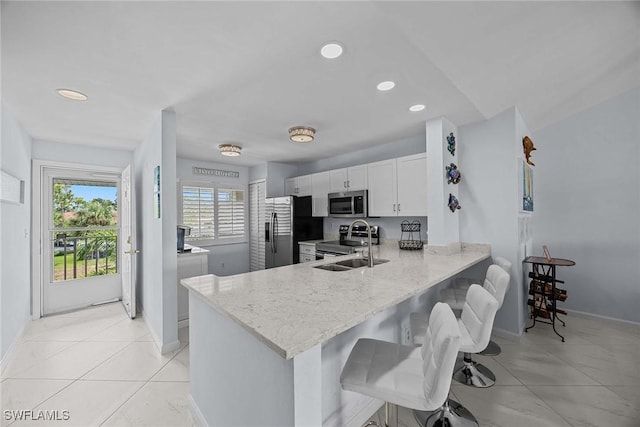 kitchen featuring stainless steel appliances, a sink, a peninsula, and light stone countertops