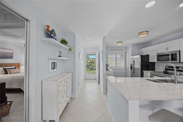 kitchen with stainless steel appliances, light stone counters, a sink, and white cabinetry