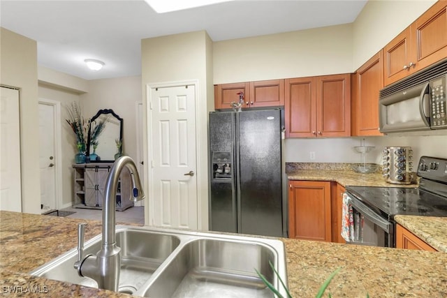 kitchen featuring black appliances, light stone counters, brown cabinetry, and a sink