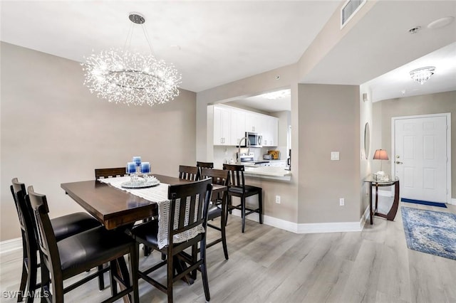 dining area featuring a notable chandelier, baseboards, visible vents, and light wood-style floors