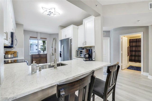 kitchen with stainless steel appliances, tasteful backsplash, light stone countertops, a peninsula, and a kitchen bar