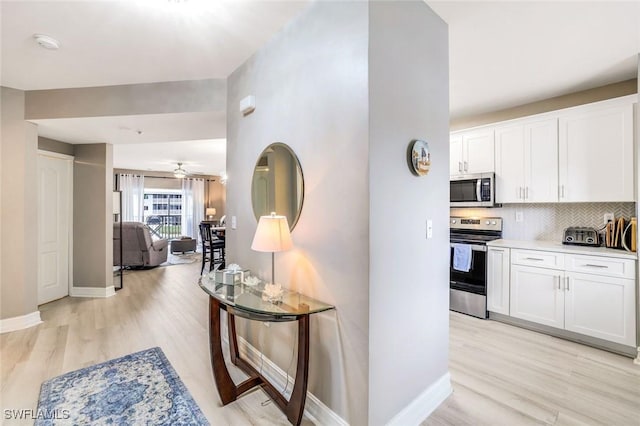 kitchen featuring white cabinets, light wood finished floors, tasteful backsplash, and stainless steel appliances