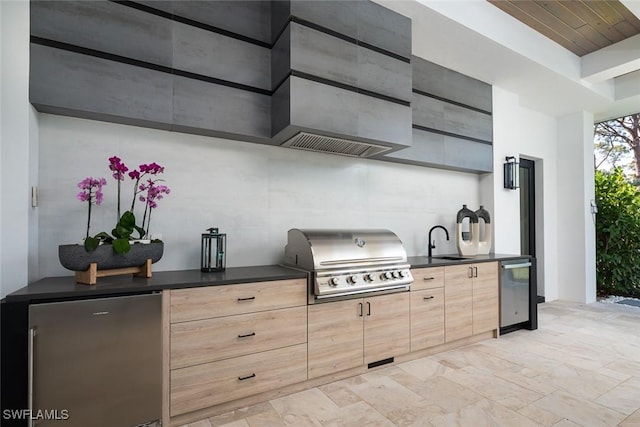 kitchen featuring dark countertops, refrigerator, freestanding refrigerator, light brown cabinets, and a sink