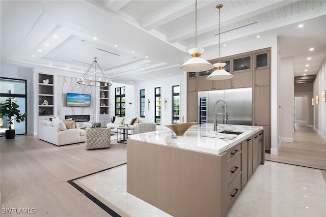 kitchen featuring a center island with sink, built in features, a fireplace, a sink, and built in fridge