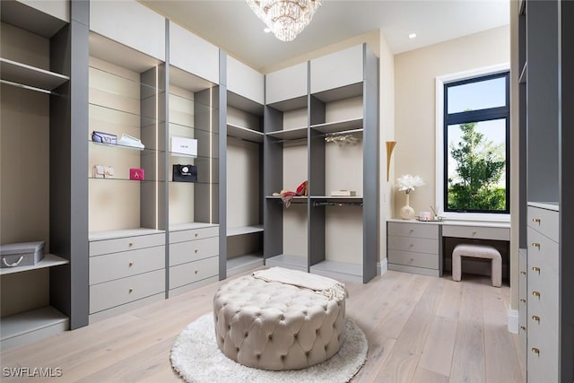 spacious closet featuring built in desk, a chandelier, and light wood-style flooring