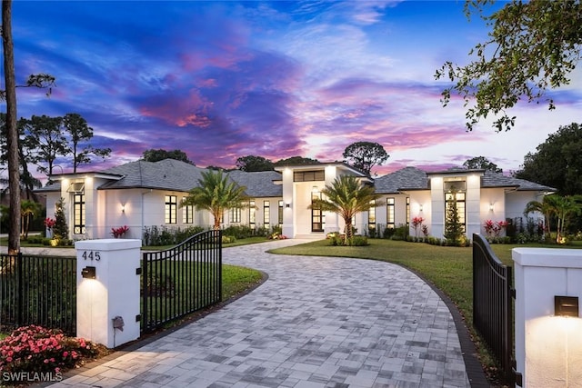 view of front of property with a fenced front yard, decorative driveway, stucco siding, a front yard, and a gate