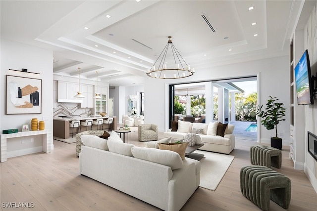 living room with light wood-style flooring, a tray ceiling, a fireplace, a notable chandelier, and recessed lighting