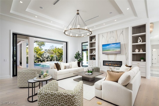 living room featuring built in shelves, a raised ceiling, and light wood-style flooring