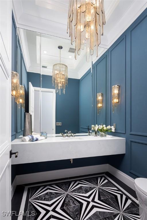 bathroom featuring a chandelier, a decorative wall, and crown molding