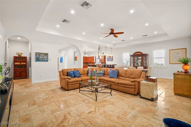 living room featuring a tray ceiling, stone tile flooring, and visible vents