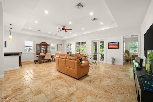 living room featuring a raised ceiling, visible vents, and stone tile floors