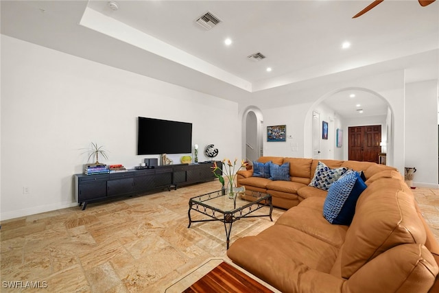 living area with visible vents, arched walkways, a raised ceiling, and a ceiling fan