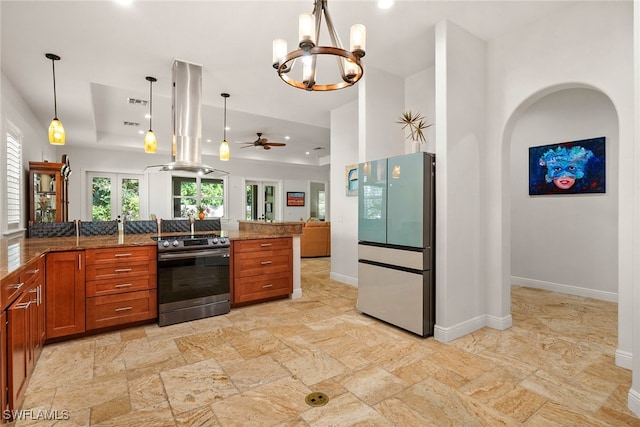 kitchen featuring a tray ceiling, island exhaust hood, stainless steel electric stove, brown cabinetry, and freestanding refrigerator