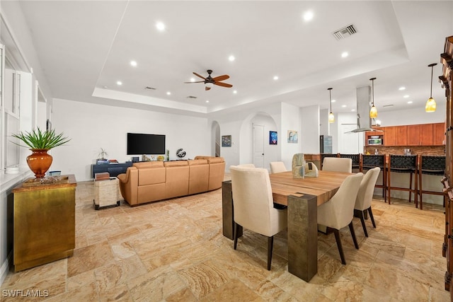 dining area featuring ceiling fan, a tray ceiling, arched walkways, and recessed lighting