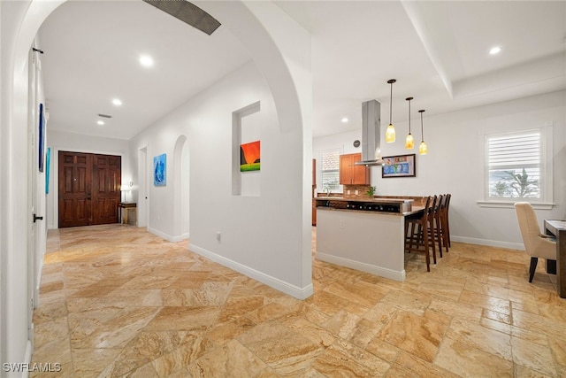 kitchen featuring arched walkways, dark countertops, a healthy amount of sunlight, island range hood, and baseboards