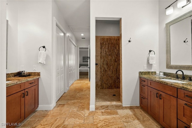 bathroom with stone finish flooring, baseboards, a tile shower, and vanity