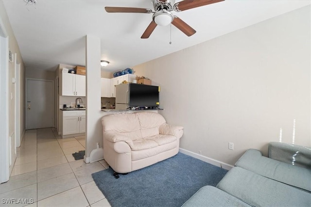 living area with light tile patterned flooring, ceiling fan, and baseboards