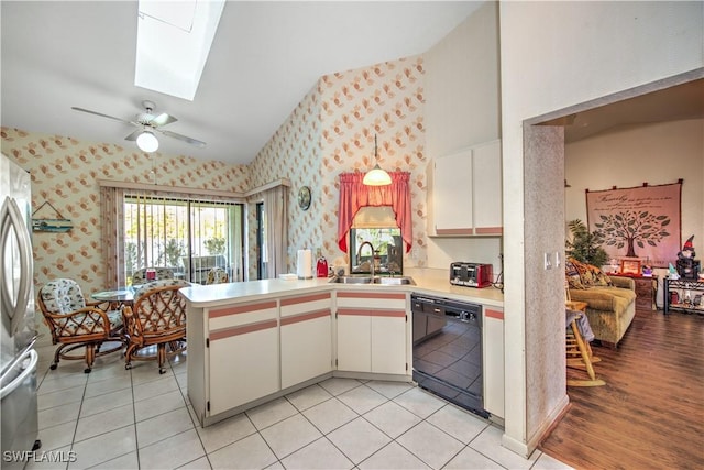 kitchen with a sink, black dishwasher, freestanding refrigerator, lofted ceiling with skylight, and wallpapered walls