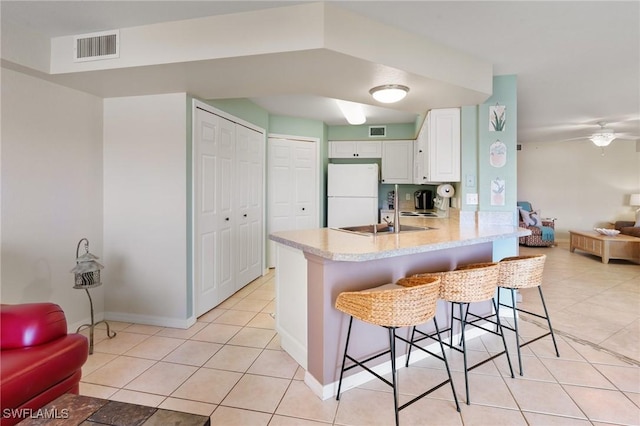 kitchen with visible vents, white cabinets, a breakfast bar area, freestanding refrigerator, and light countertops