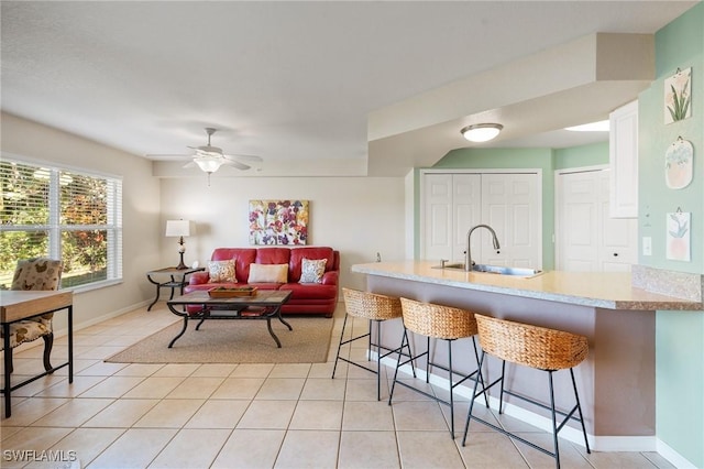 kitchen with light tile patterned floors, a breakfast bar, a sink, baseboards, and light countertops