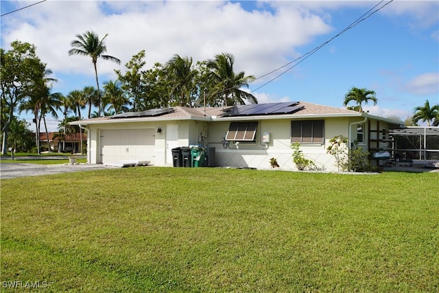 ranch-style house featuring stucco siding, a front yard, roof mounted solar panels, a garage, and driveway