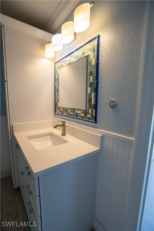 bathroom with a wainscoted wall, a textured wall, a decorative wall, and vanity