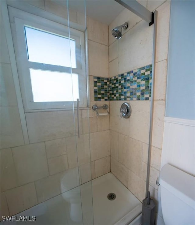 bathroom with toilet, a stall shower, and wainscoting