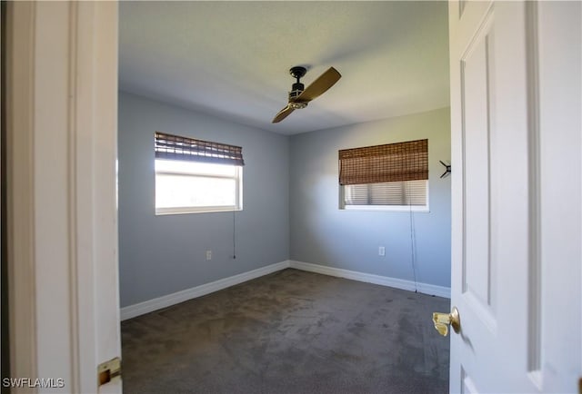 empty room featuring a ceiling fan, dark colored carpet, and baseboards