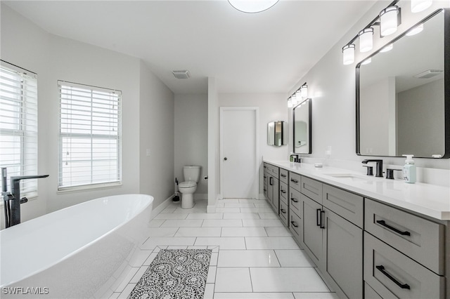 full bath featuring double vanity, visible vents, a freestanding bath, toilet, and a sink