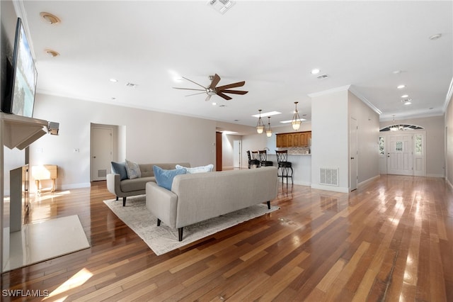 living room with ornamental molding, light wood-type flooring, visible vents, and baseboards