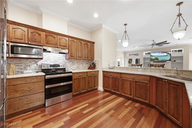 kitchen featuring stainless steel appliances, hanging light fixtures, brown cabinetry, a sink, and under cabinet range hood