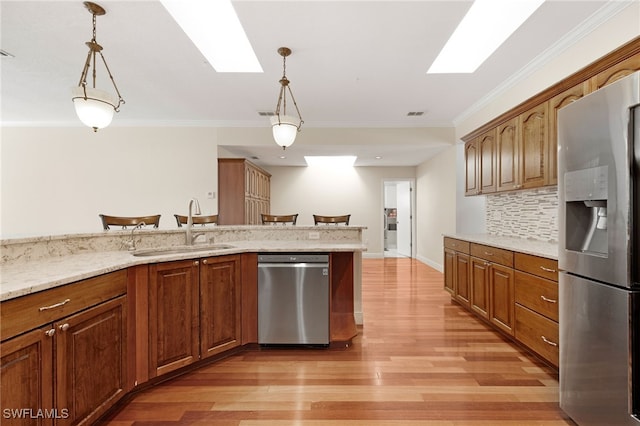 kitchen featuring a skylight, hanging light fixtures, stainless steel appliances, light wood-type flooring, and a sink