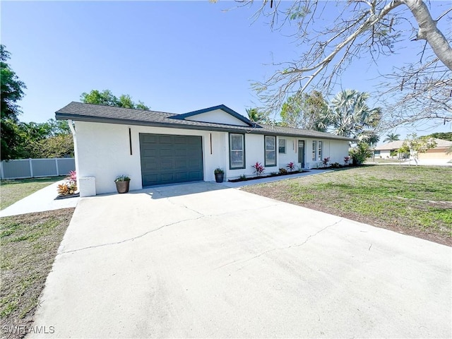 ranch-style home featuring an attached garage, fence, driveway, stucco siding, and a front lawn