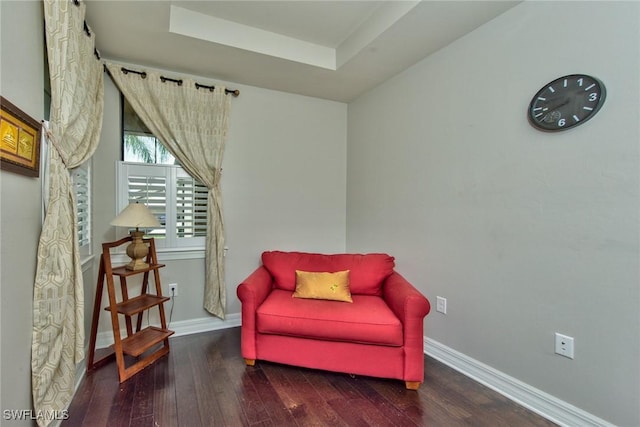 living area with a tray ceiling, dark wood finished floors, and baseboards