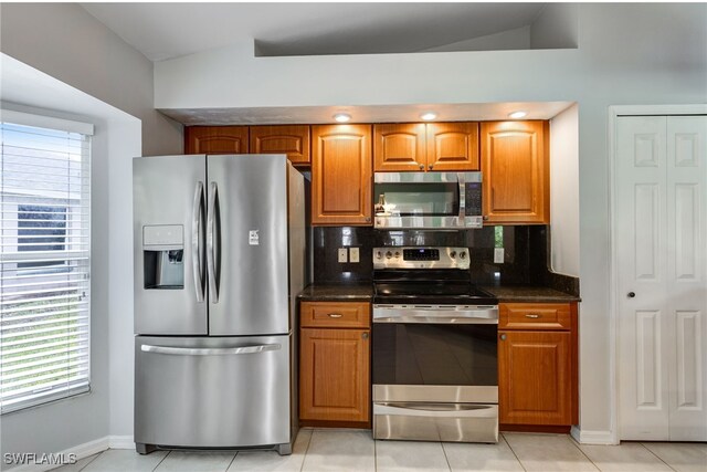 kitchen featuring light tile patterned floors, dark stone counters, brown cabinets, stainless steel appliances, and backsplash