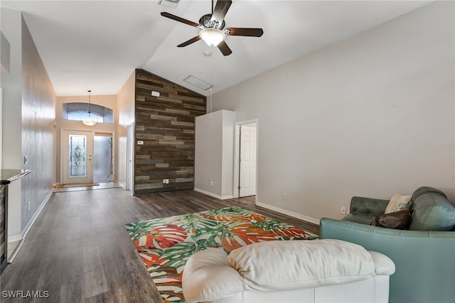 living area with high vaulted ceiling, an accent wall, wood walls, wood finished floors, and baseboards