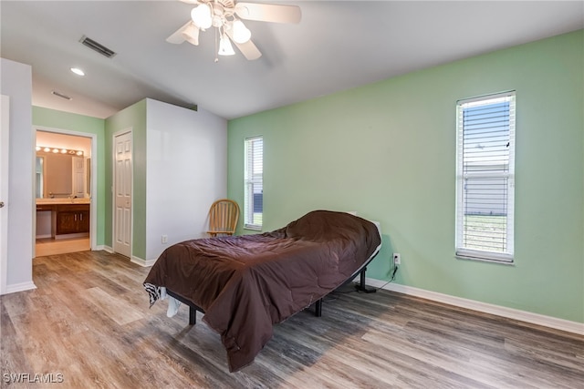 bedroom featuring visible vents, ensuite bath, baseboards, and wood finished floors