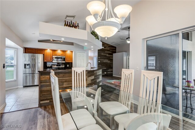 dining room with lofted ceiling, light tile patterned flooring, ceiling fan with notable chandelier, visible vents, and baseboards