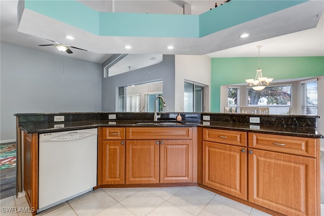 kitchen featuring white dishwasher, a sink, vaulted ceiling, brown cabinets, and dark stone counters