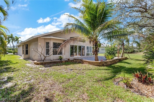 rear view of property featuring a lawn, a patio, and stucco siding