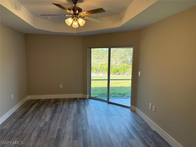 unfurnished room featuring dark wood-style floors, baseboards, a tray ceiling, and a ceiling fan