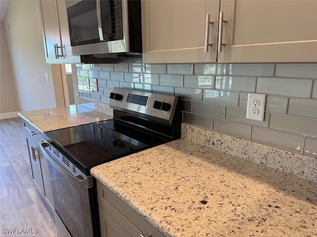 kitchen with stainless steel appliances, baseboards, light wood-style floors, light stone countertops, and tasteful backsplash