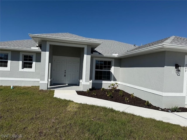 property entrance featuring roof with shingles, a lawn, and stucco siding