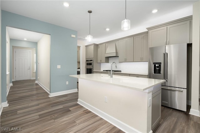 kitchen with a center island with sink, appliances with stainless steel finishes, light countertops, gray cabinetry, and premium range hood