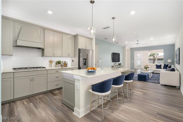 kitchen with appliances with stainless steel finishes, open floor plan, light countertops, and an island with sink