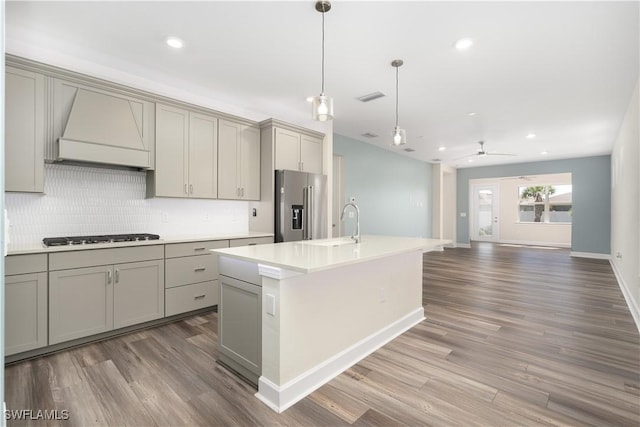 kitchen with an island with sink, custom exhaust hood, stainless steel appliances, light countertops, and gray cabinetry