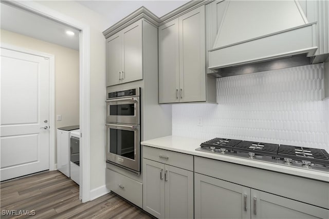 kitchen with washing machine and clothes dryer, stainless steel appliances, gray cabinets, light countertops, and custom range hood